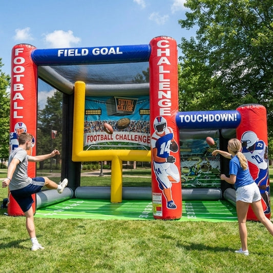 Inflatable football challenge game being played outdoors at an event on a grassy area with trees in the background.