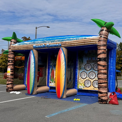 Inflatable beach-themed game booth with palm trees and surfboards in a parking lot at an event.