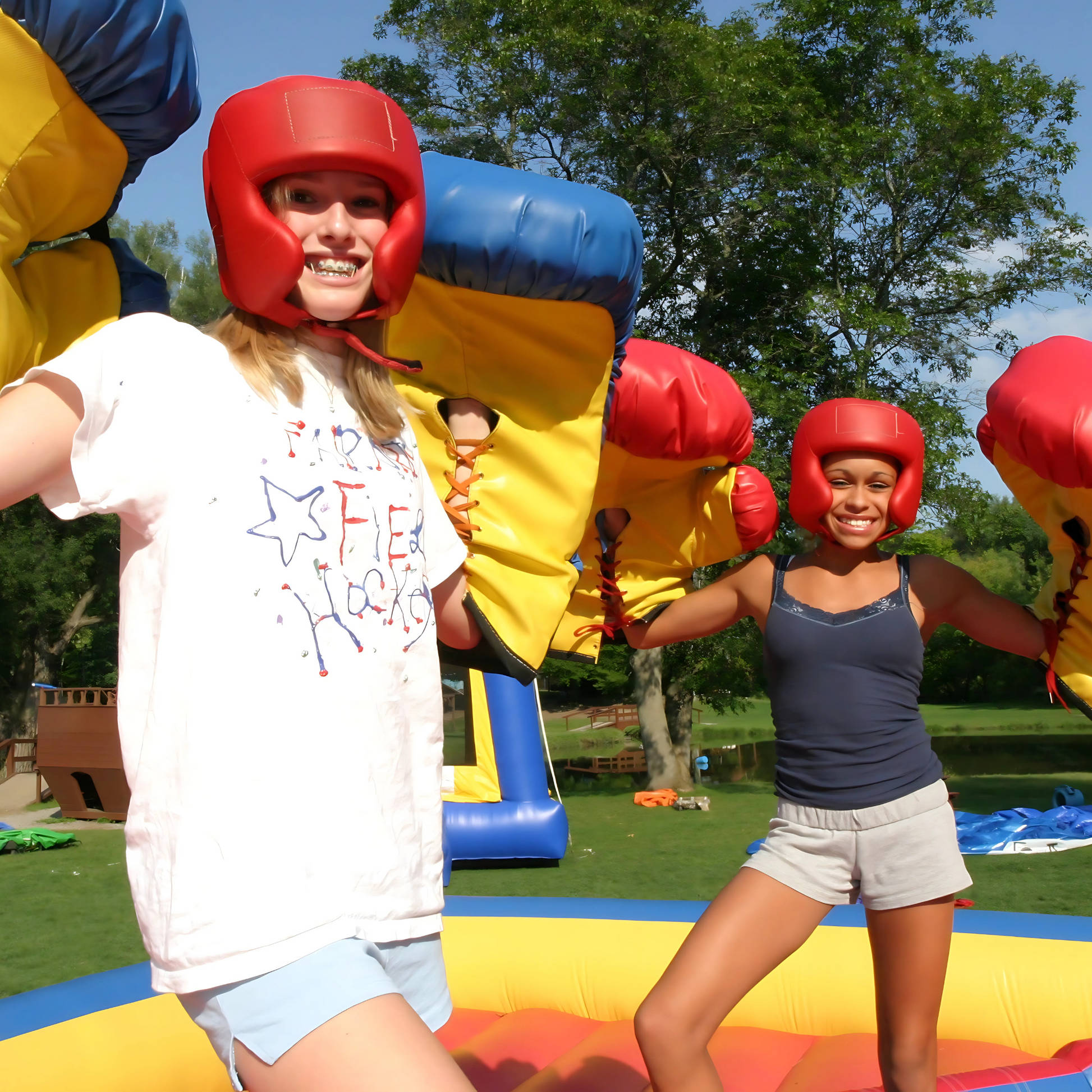 Two players wearing oversized boxing gloves and protective headgear on the Bouncy Boxing Inflatable