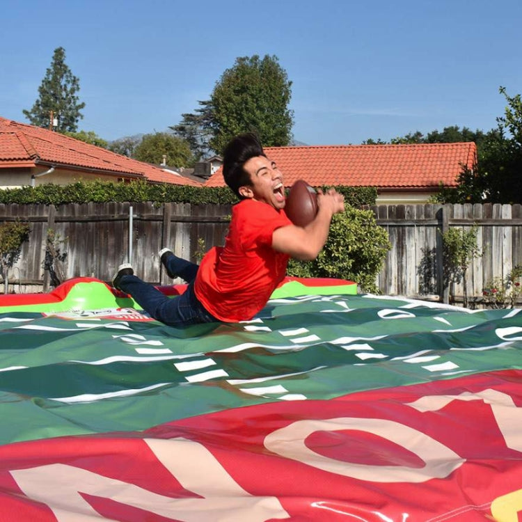 Person catching a football mid-air before landing on an inflatable.
