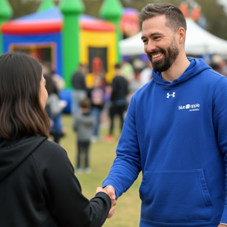 Blue Apple Productions employee shaking customer's hand in front of a bounce house at an event in Rochester, NY.