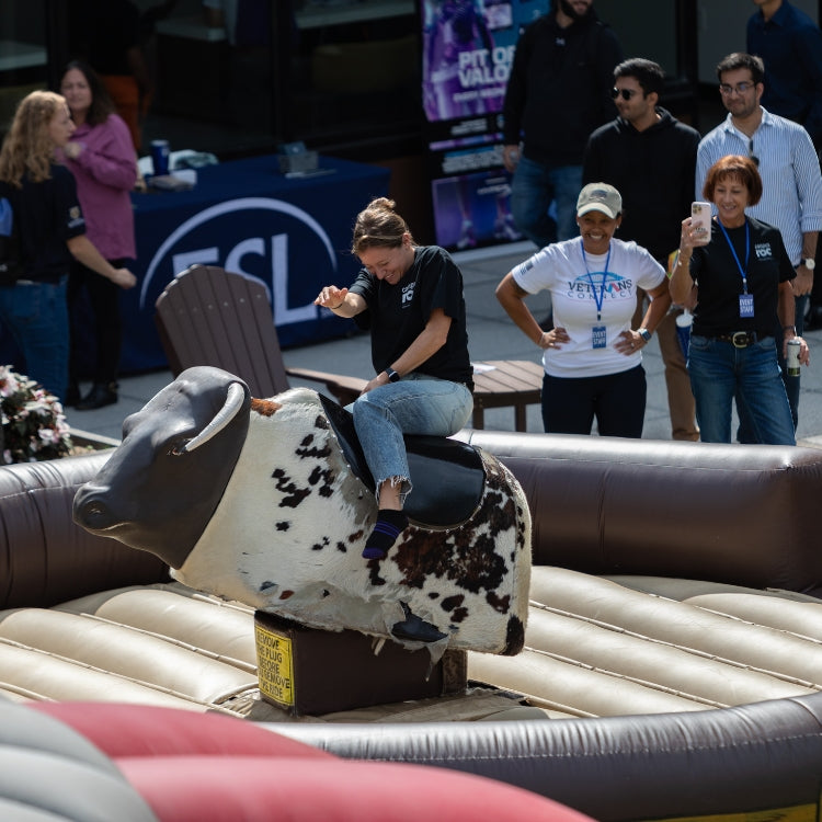 Woman Riding Mechanical Bull Rental While Others Watch at Event in Rochester, NY