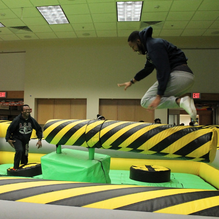 Man Leaping Over Meltdown Zone Mechanical Arm Before Landing on Inflatable Base Below at Event in Rochester, NY